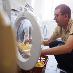 Ein junger Mann holt Wäsche aus der Waschmaschine